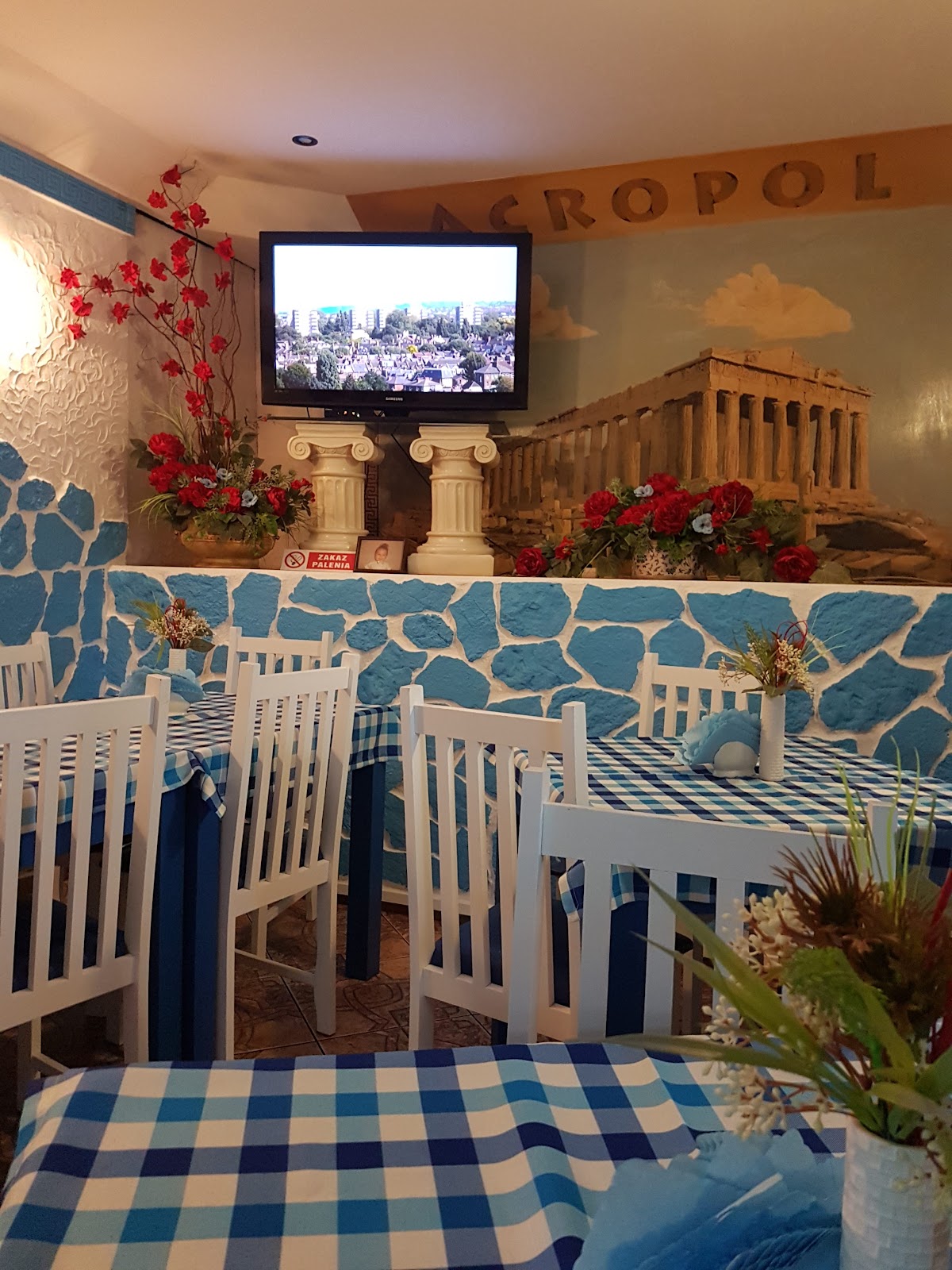 Wnętrze Bar Akropol w Lubinie z muralem Akropolu, białymi kolumnami i niebiesko-białymi obrusami w kratę